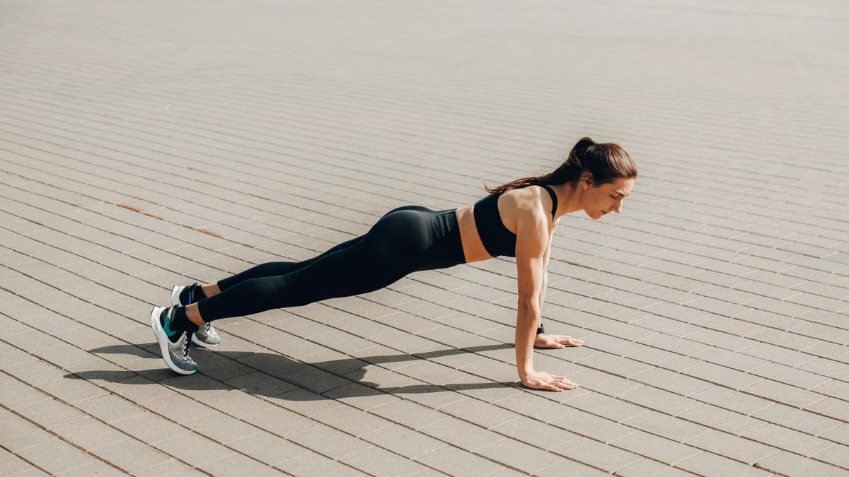 Woman doing push-ups outdoors in activewear, promoting fitness and healthy lifestyle.